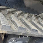 Close-up of dusty, cracked black track links on heavy equipment, with a metal frame and bolts visible behind it.