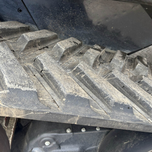 Close-up of dusty, cracked black track links on heavy equipment, with a metal frame and bolts visible behind it.