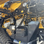 Close-up of a yellow industrial machine’s interior showing belts, pulleys, hoses and metal framework.