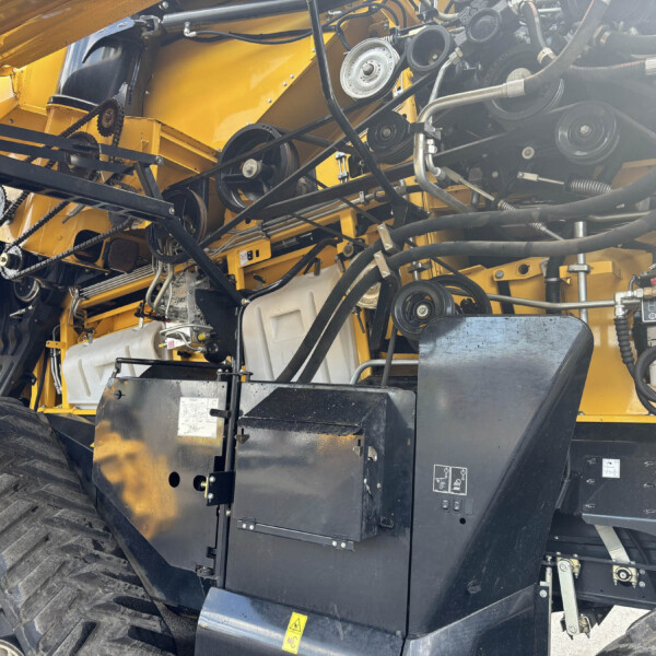 Close-up of a yellow industrial machine’s interior showing belts, pulleys, hoses and metal framework.