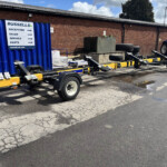 Blue shipping container beside a brick wall with a large Russell's sign listing reception, sales, service, and parts; trailer under construction with a blue tractor at the far end.