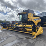 Yellow New Holland combine harvester with front header in an outdoor equipment yard under cloudy skies.
