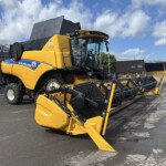 Yellow New Holland combine harvester parked in a yard under a blue sky with clouds.