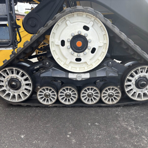 Close-up side view of a heavy tracked machine’s large white drive wheel and rubber track, with yellow machinery in the background and gray body panels behind.