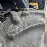 Close-up of a muddy, large tractor tire with hydraulic hoses and metal framework in the background of a heavy-duty machine.