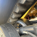 Close-up of large, dirt-smeared tires and a yellow heavy-machinery frame showing bolts and suspension components.