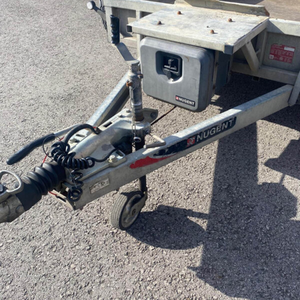 Tow trailer hitch with coiled electrical cables and a gray tool box labeled NUGENT on a sunny asphalt lot