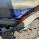 Blue metal identification plate on a trailer frame reading KNOTT GmbH, model and serial numbers, with a red cable crossing in front.