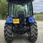 Rear view of a blue tractor with a yellow RUSSELLS sign, orange beacon, and large rear tires in a farmyard.