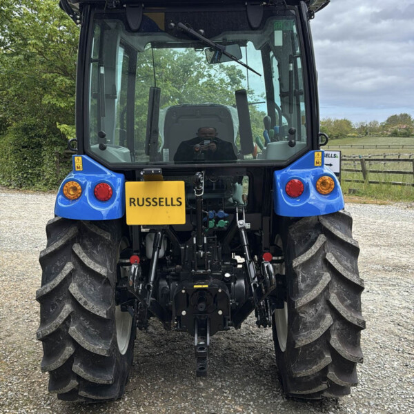 Rear view of a blue tractor with a yellow RUSSELLS sign, orange beacon, and large rear tires in a farmyard.
