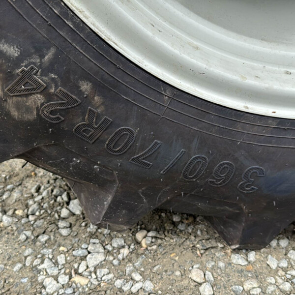 Close-up of a large, muddy off-road tire with a white wheel rim on a gravel surface.