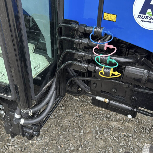 Close-up of blue machinery showing hydraulic hoses and color-coded quick-connect plugs (blue, pink, green, yellow) at a maintenance point.