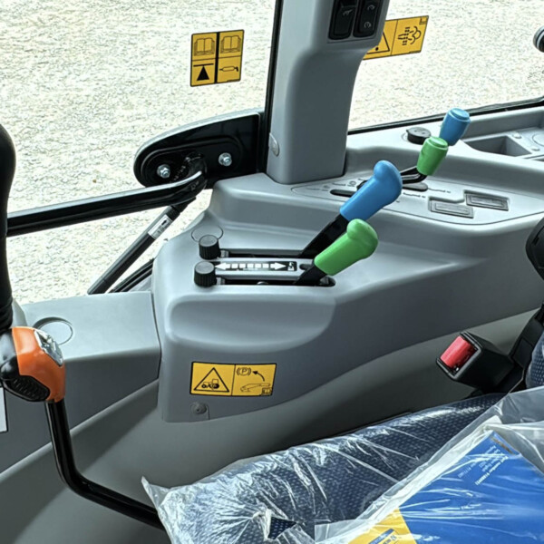 Interior of a tractor cab showing colorful gear levers (blue, green) and control panel with yellow warning decals behind the windshield.
