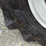 Close-up of a black tire on a light-colored rim, showing tread grooves and dirt on a rocky surface.