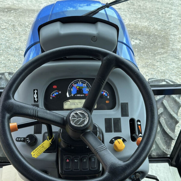 Inside the cab of a blue tractor, viewed from the driver's seat with steering wheel and dashboard gauges ahead.