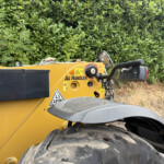 Close-up of a yellow construction vehicle with oversized tires parked beside a dense green hedge.