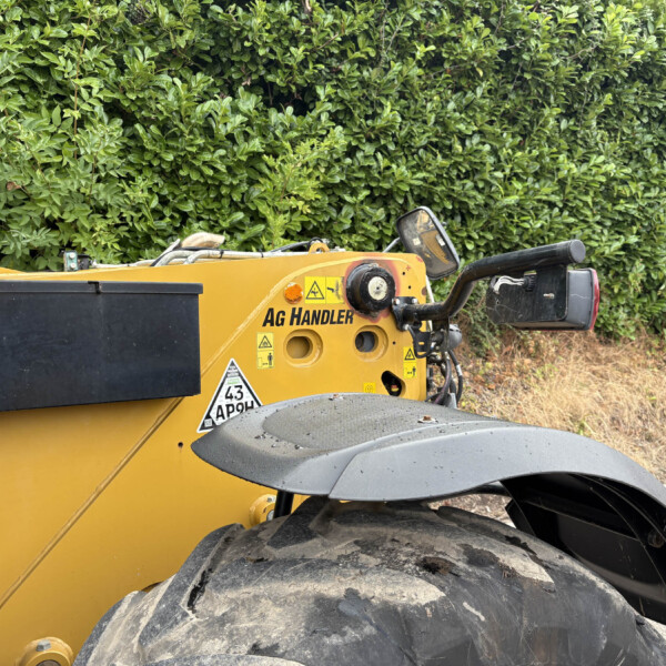 Close-up of a yellow construction vehicle with oversized tires parked beside a dense green hedge.
