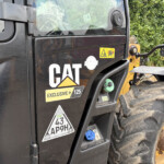 Close-up of a black CAT construction truck side with warning decals and a dirt-covered tire nearby.
