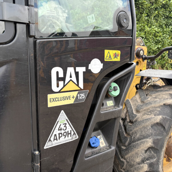 Close-up of a black CAT construction truck side with warning decals and a dirt-covered tire nearby.