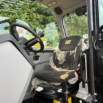 Interior of a construction vehicle cab with a heavily torn fabric seat covered in plastic, showing exposed foam and wear near the base; steering wheel and warning labels visible.