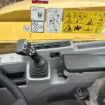 Interior of a yellow construction machine cab with multiple safety instruction stickers and a joystick/control panel visible