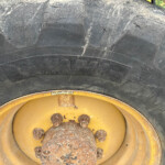 Close-up of a large, dirty tire on a yellow wheel with rusty lug nuts and visible wear on the tread edge.