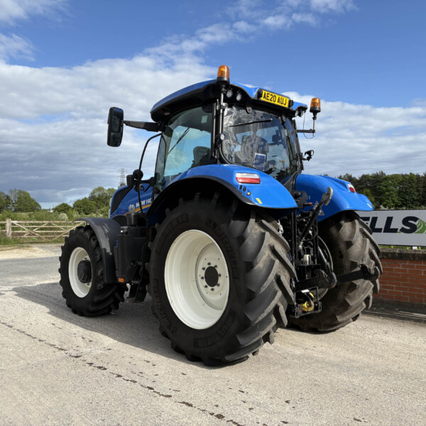 Blue agricultural tractor seen in a parking area, front-left angle with oversized tires and orange beacon lights on top panel license plate AE20 AJJ
