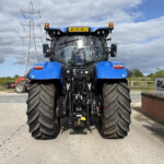 Front view of a blue agricultural tractor with oversized tires, orange beacon lights, and a Russell sign in the background.
