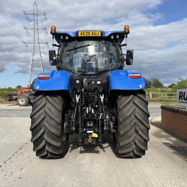 Front view of a blue agricultural tractor with oversized tires, orange beacon lights, and a Russell sign in the background.
