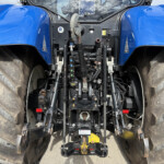 Close-up view of a blue tractor’s rear cab area, showing hydraulic levers, linkages, and controls between oversized tires.