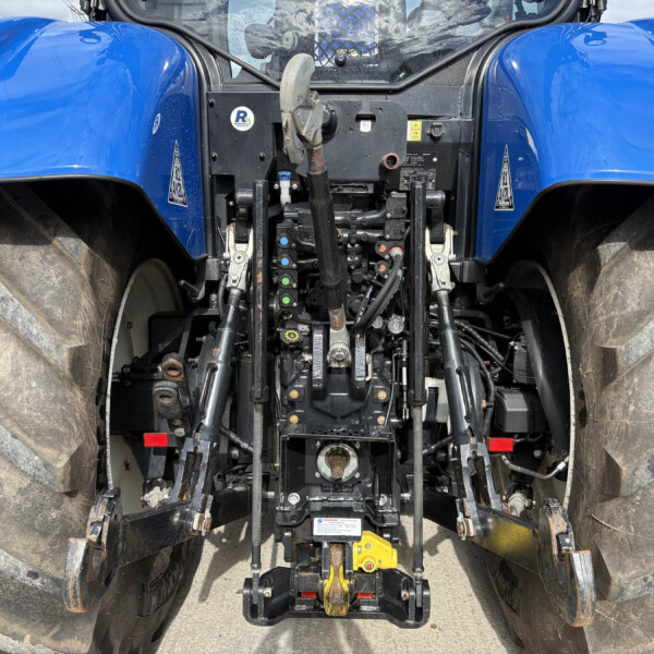 Close-up view of a blue tractor’s rear cab area, showing hydraulic levers, linkages, and controls between oversized tires.