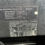 Metal identification plate on a dark, wet surface showing CNH Industrial Italia S.p.A. and Made in UK with model/approval details.