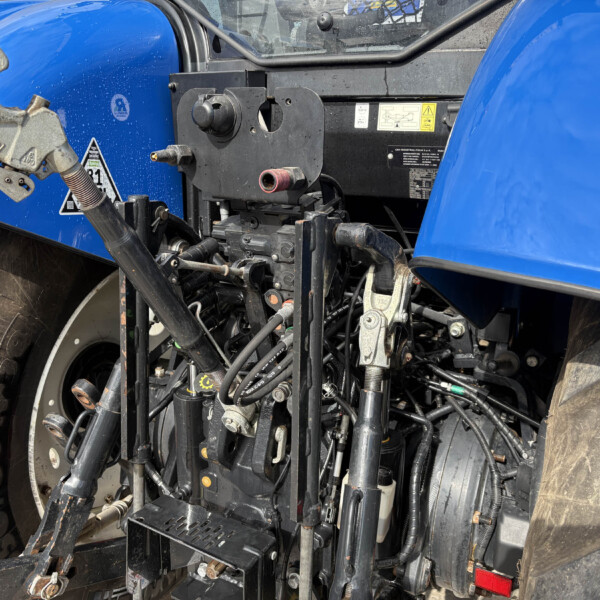 Close-up of hydraulic controls and linkage on a blue tractor, with hoses and a red hydraulic plug visible