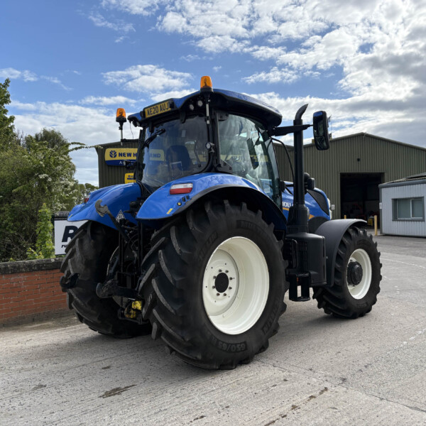 Blue New Holland tractor with oversized white wheels parked outdoors beside a warehouse under a partly cloudy sky.