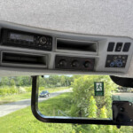 Dashboard of a vehicle cabin with a radio, climate controls, and small storage compartments; raindrop-speckled windshield shows a sunny outdoor scene outside.