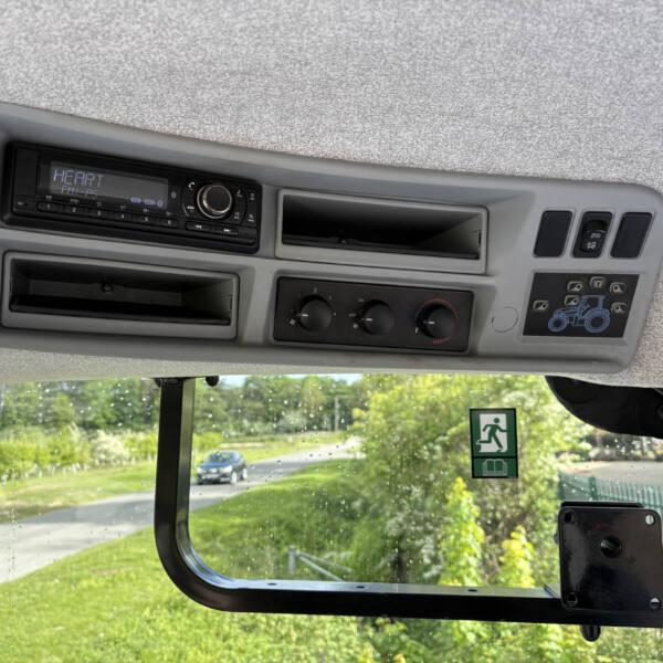 Dashboard of a vehicle cabin with a radio, climate controls, and small storage compartments; raindrop-speckled windshield shows a sunny outdoor scene outside.