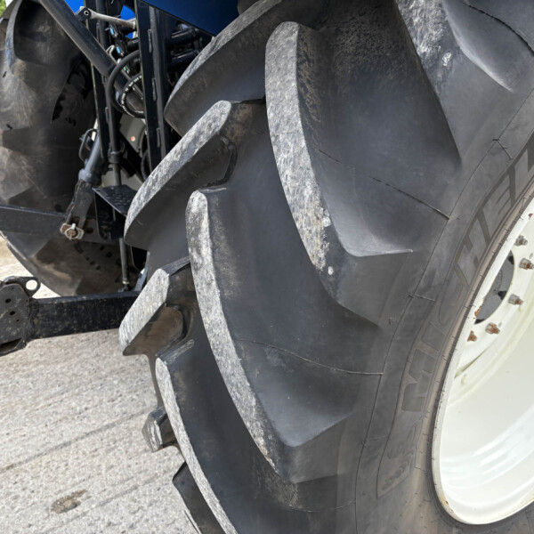 Close-up of a large heavy-duty tractor tire with a hitch in an outdoor setting, showing rugged treads and dirt marks.