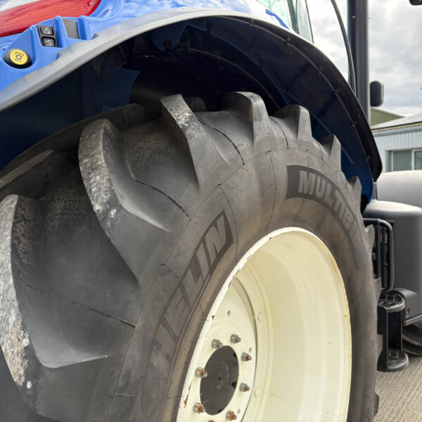 Close-up of a large tractor tire with blue bodywork and a red taillight visible above the wheel.