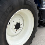 Close-up of a large tractor tire with a white rim and rust on the lug nuts.