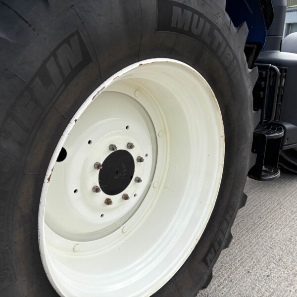 Close-up of a large tractor tire with a white rim and rust on the lug nuts.