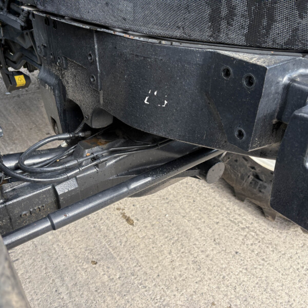 Close-up of a dirty black vehicle frame with hoses and wiring beneath the undercarriage of a truck/piece of heavy machinery.