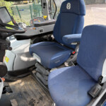 Interior of a tractor cab with blue fabric seats, steering wheel, and the dashboard with many controls visible behind the seatheadrest.