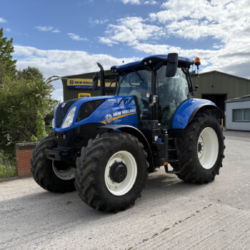 Blue New Holland tractor parked outdoors in front of an agricultural building with a New Holland Agriculture sign visible on the façade.