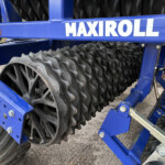 Blue agricultural implement with large black ridged rollers mounted on a metal frame.