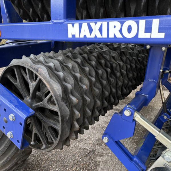 Blue agricultural implement with large black ridged rollers mounted on a metal frame.