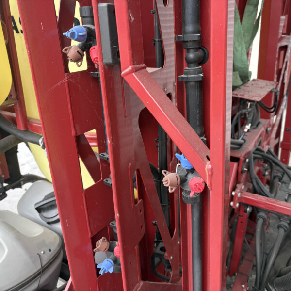 Close-up of a red metal frame with hoses, valves and blue/brown quick-connect fittings; a yellow reservoir sits behind the frame.
