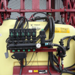Industrial machinery with a yellow tank, red metal frame, and numerous hoses and gauges mounted in a truck or trailer tray.