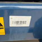Blue metal container with a yellow caution sticker and a white barcode label on its surface.