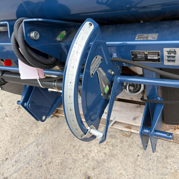 Close-up of blue agricultural machinery with a vertical measurement scale marked 0–8, attached near a hinge and hoses.