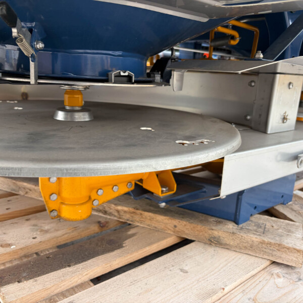 Underside view of industrial machinery mounted on a wooden pallet, showing blue frame, yellow support components, and metallic brackets.